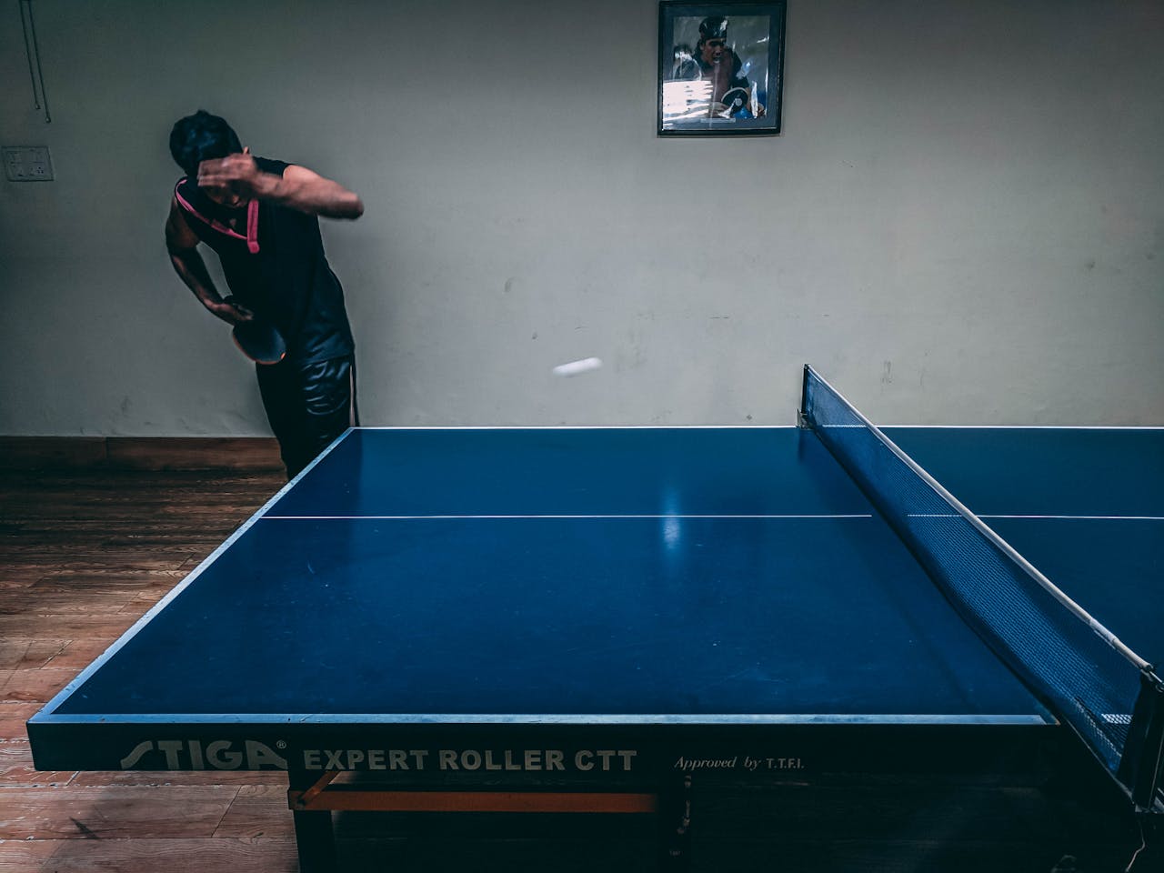 services-04 Dynamic action shot of a man playing table tennis indoors, capturing a moment of intense focus and skill.